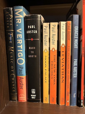 A row of books by Paul Auster, including The Music of Chance, Mr Vertigo, Hand to Mouth, Moon Palace, The New York Trilogy, Leviathan, The Invention of Solitude and Oracle Night. 